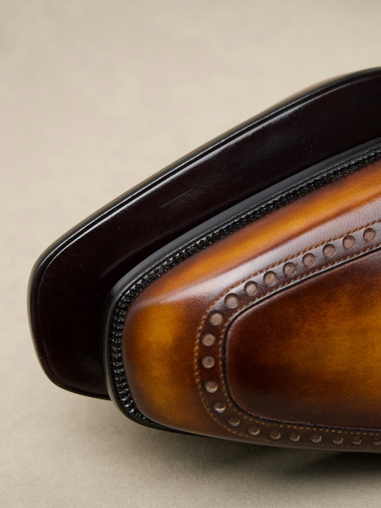 Close-up of a brown leather wingtip shoe showing the toe cap, brogue detailing, and dark sole edge against a neutral beige background.