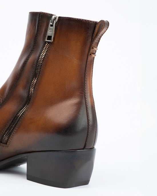 A close-up side view of a brown leather ankle boot with a side zipper, low block heel, and dark sole, shown against a plain white background.