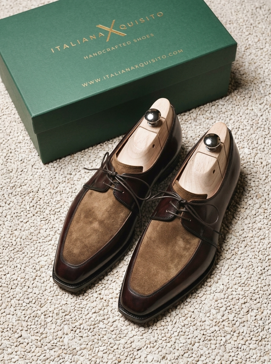 A pair of Italian X Quisito handcrafted shoes in dark brown suede and glossy leather, displayed on wooden shoe trees next to their green branded box on a textured beige carpet.