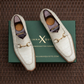 A pair of off-white crocodile-embossed loafers with gold horsebit detailing, displayed on top of a green shoebox on a brown woven mat background.